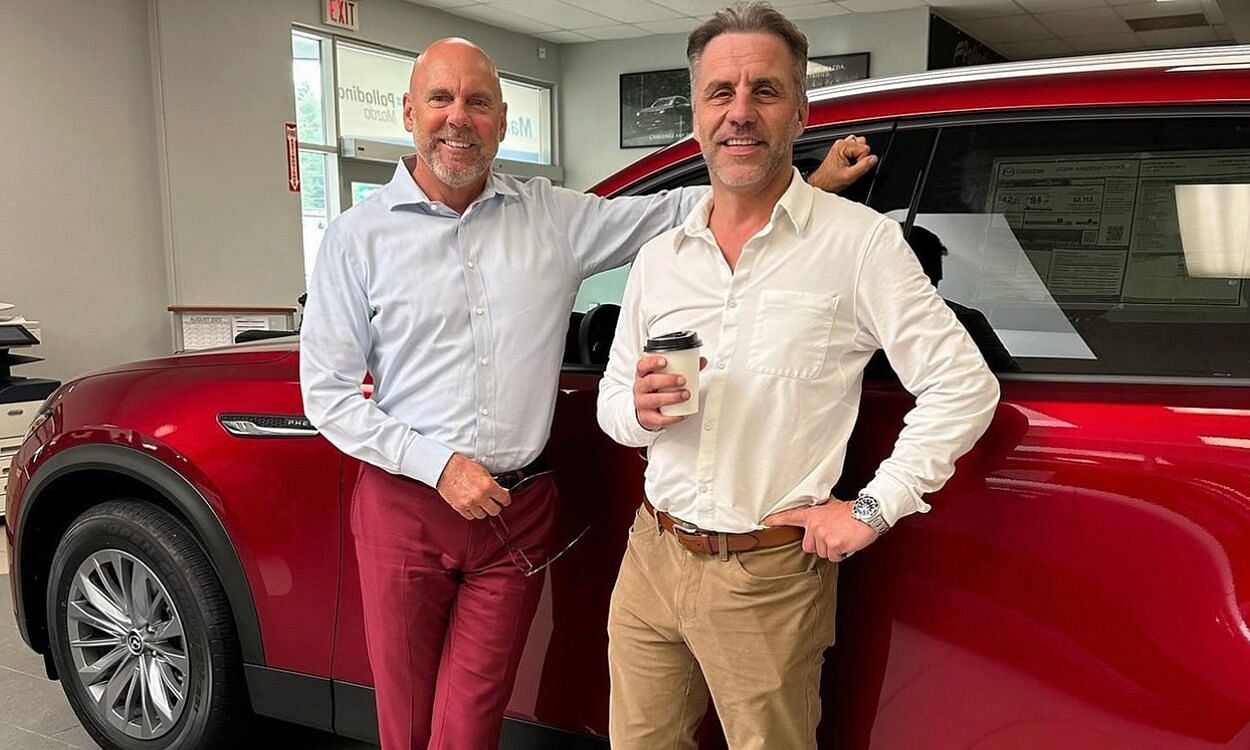 Two people in white shirts standing by a red car