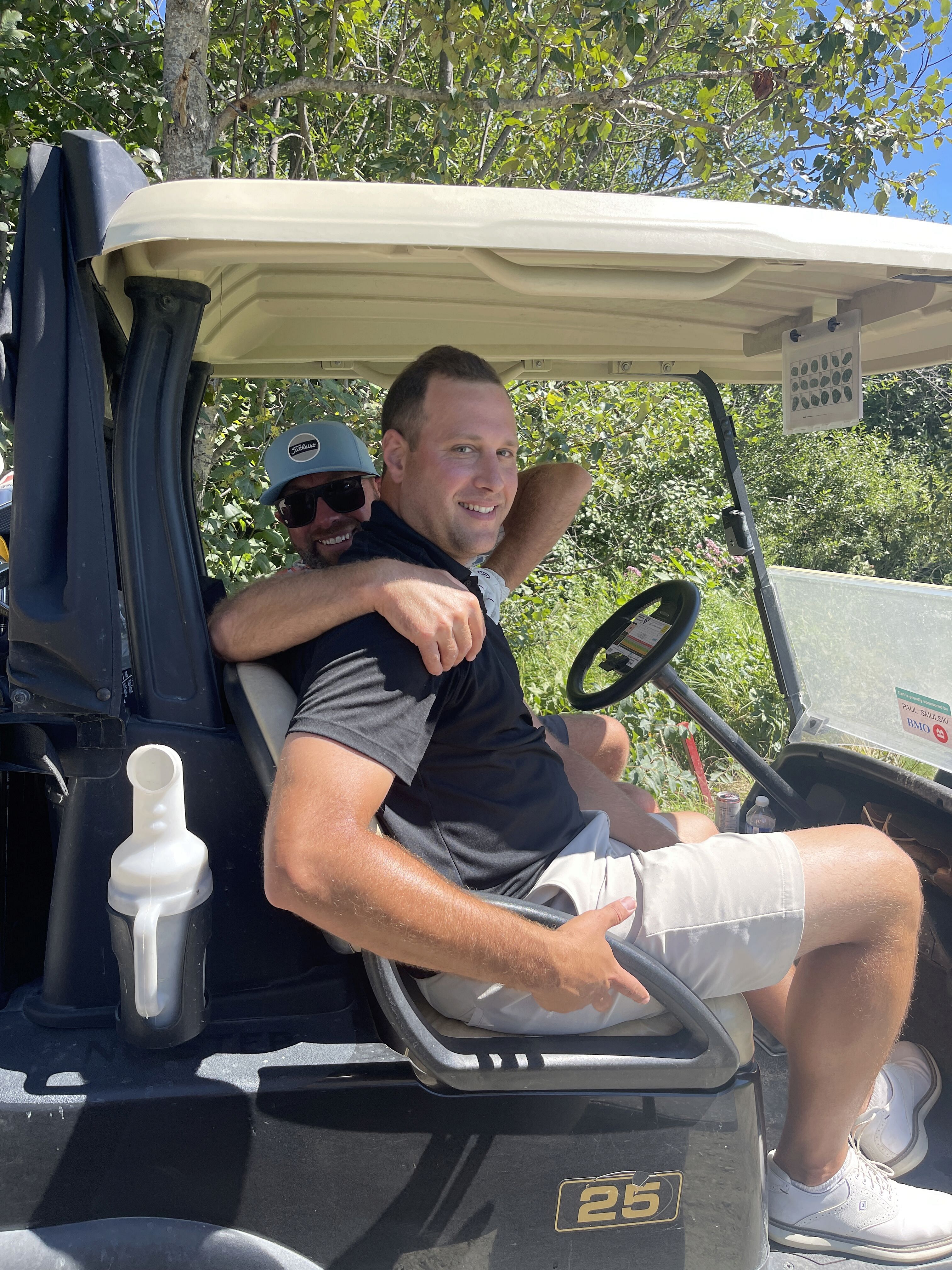 Two smiling men in a golf cart.